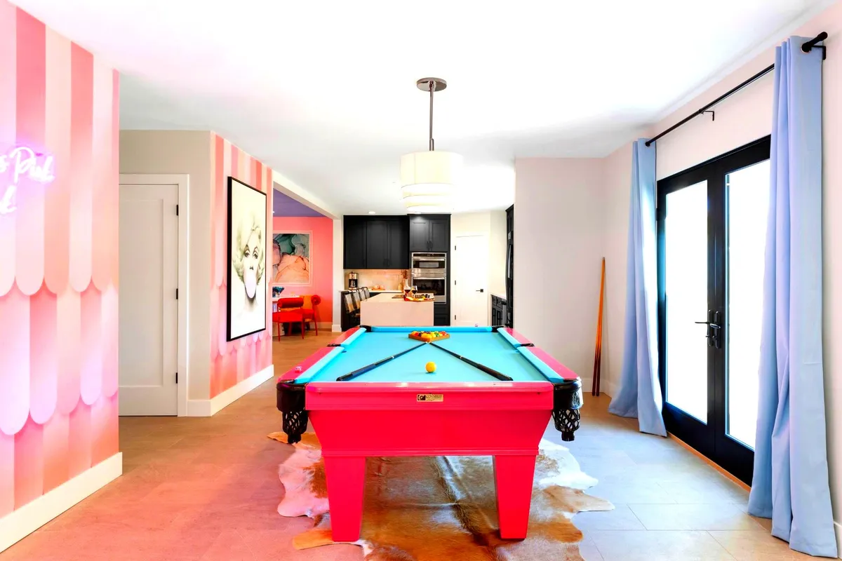 A lively entertainment area featuring a pink pool table, neon sign, and vibrant artwork, surrounded by cozy seating. The space invites guests to play, socialize, and enjoy the unique, photogenic atmosphere.