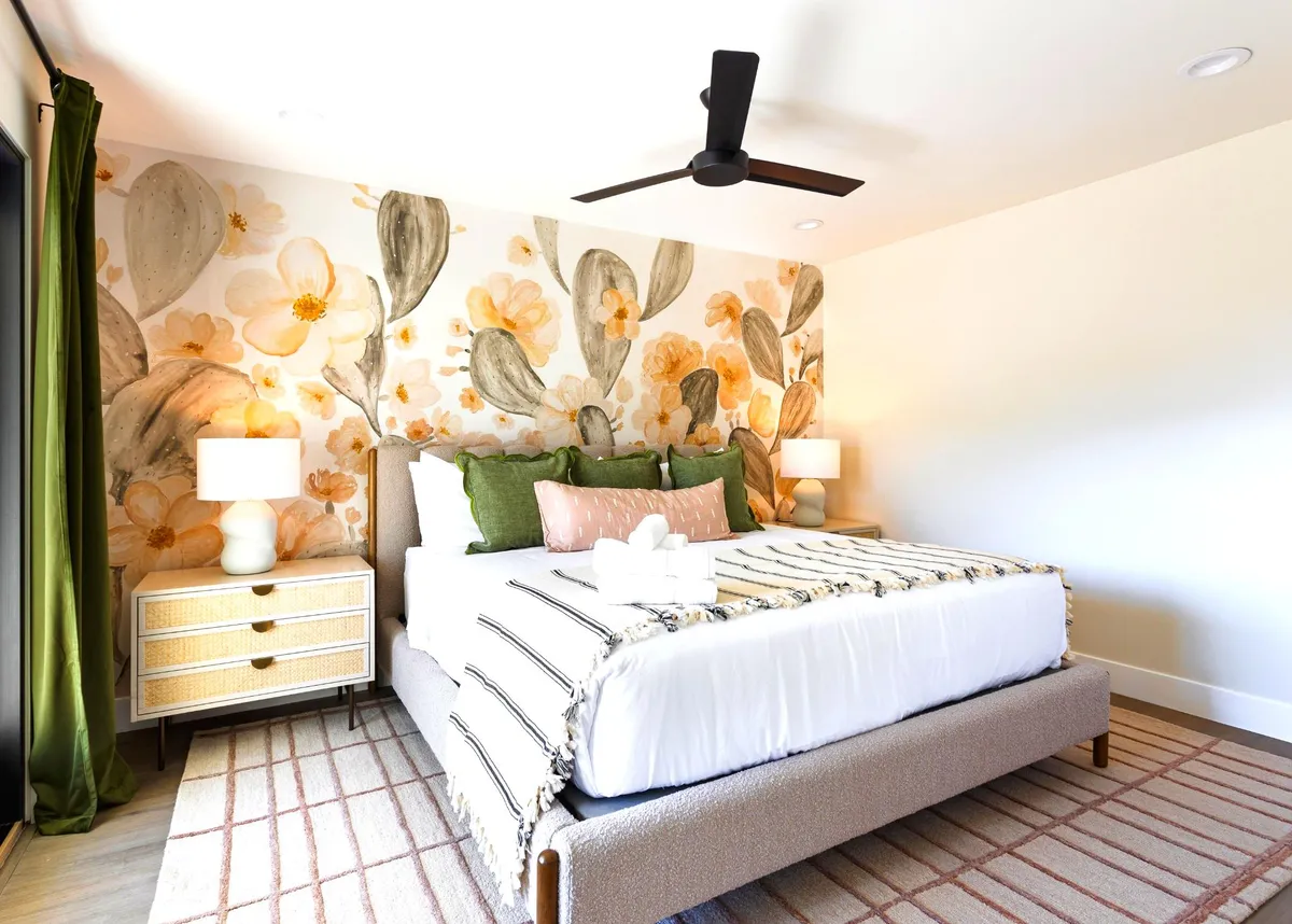 A serene bedroom with floral wallpaper, a plush bed adorned with decorative pillows, and nightstands with matching lamps. The room is softly lit, creating a restful, elegant ambiance ideal for relaxation or reading. The décor blends comfort with a touch of feminine glam.
