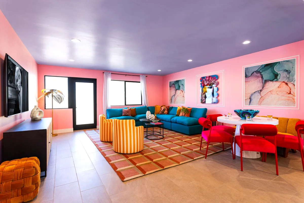 A vibrant interior living and dining space with a colorful sectional sofa, unique accent chairs, eye-catching artwork, and a dining table. The room is styled for both comfort and social interaction, ideal for hosting family or group events.