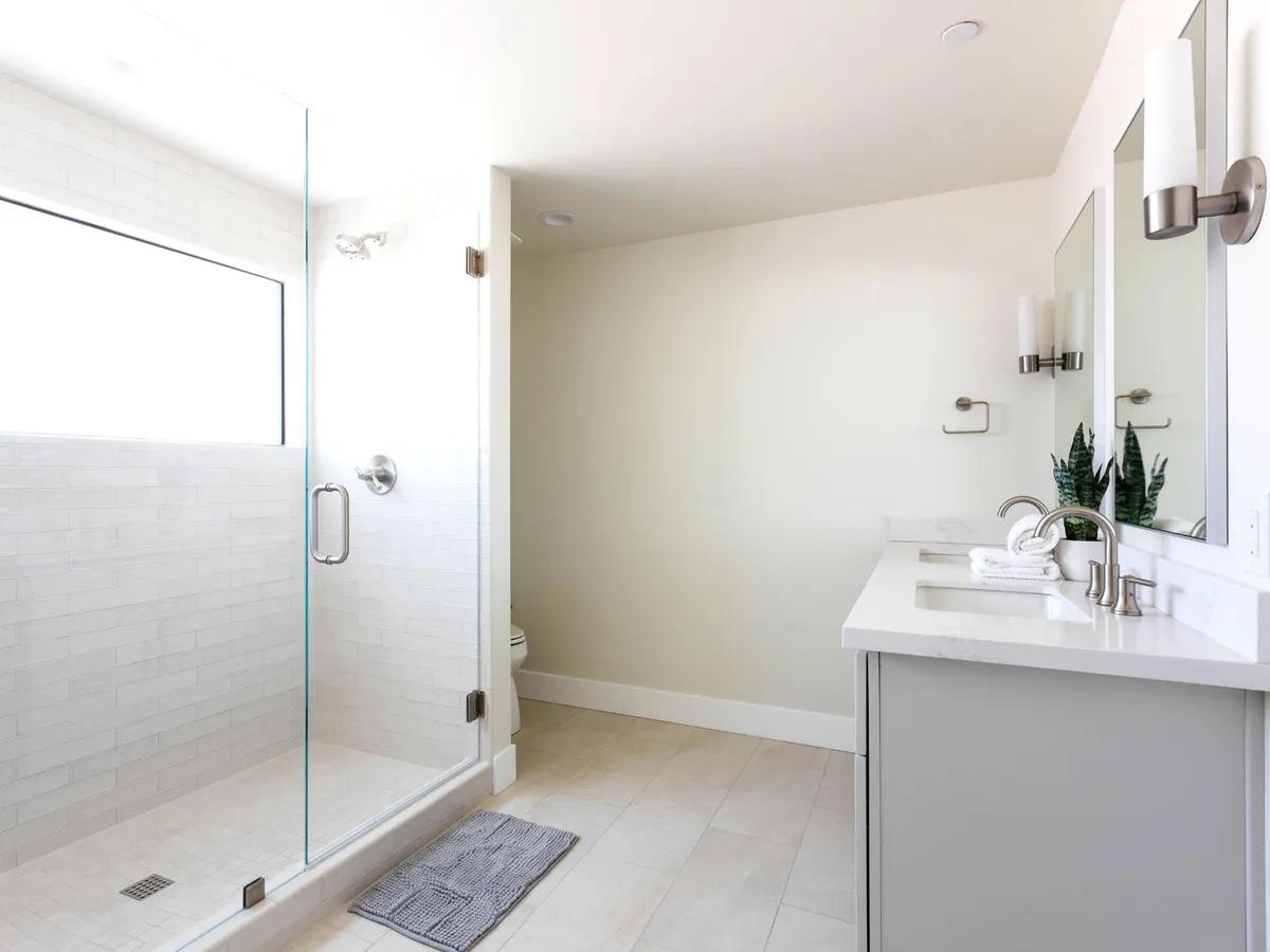 A spacious, modern bathroom featuring a glass shower enclosure, double sink vanity, and a large window that fills the space with natural light. The clean design and ample amenities evoke spa-like tranquility and convenience.
